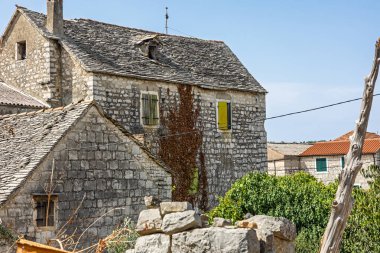 Tuhaf kireçtaşı evler, engebeli taş duvarları, açıkta çatıları ve güneşli gökyüzü olan küçük bir köy manzarası oluşturur. Kültür, gelenek ve basit ülke yaşamını çağrıştıran barışçıl ve zamansız bir ortam..