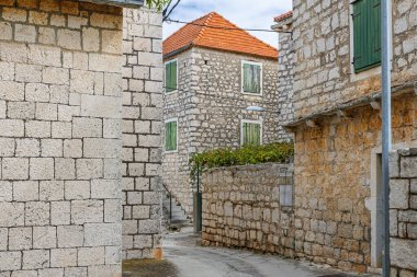 Güneşli, dar bir sokak rüzgarı, tahtadan kepenkleri ve kiremitli çatıları olan tarihi taş evler arasında sakin, kırsal bir köy atmosferi ve zamansız mimari cazibeyi yakalıyor.