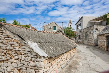 Idyllic kırsal kesimde, canlı mavi gökyüzünün altında yeşil ile çevrili bir kilise kulesinin bulunduğu taştan yapılmış büyüleyici bir köy sergileniyor..