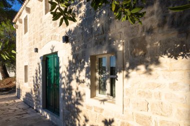 NECUJAM, CROATIA, 09.01.2025: Bir taş bina duvarında kırmızı, beyaz ve mavi kurdeleli bir çelenk ile bir hatıra plaketi barındırır. Güneşli adımlar ve derin mavi bir gökyüzü sakin tarihi bir sokak sahnesini canlandırıyor..