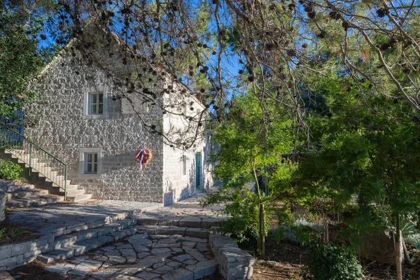 NECUJAM, CROATIA, 09.01.2025: Bir taş bina duvarında kırmızı, beyaz ve mavi kurdeleli bir çelenk ile bir hatıra plaketi barındırır. Güneşli adımlar ve derin mavi bir gökyüzü sakin tarihi bir sokak sahnesini canlandırıyor..