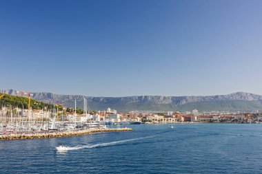 BÖLÜM, CROATIA, 09.06.2025: Teknelerin ve etrafındaki orman tepelerinin yer aldığı bir sahil şehrinin arka planına karşı Marina.