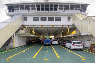 ROGAC, CROATIA, 10.22.2025: Yoğun bir araç yolculuğunda arabalar feribot güvertesi hizasında. Yeşil kat, parlak sarı işaretler ve birden fazla park etmiş araba kalabalık bir endüstriyel seyahat sahnesi yaratıyor..