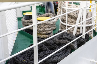 Yeşil bir güvertede kalın halat bobinleri, beyaz korkuluklar ve parlak sarı kalınlar içeren bir deniz manzarası. Düzenleme deniz işi, güç ve endüstriyel deniz atmosferini taşır.