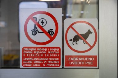 İki uyarı levhası halka açık bir salonda elektrikli scooter ve köpeklere yasak olduğunu gösteriyor. Kırmızı daireler ve kesme işaretleri bölgede güvenlik ve erişim için açık kuralları iletir.