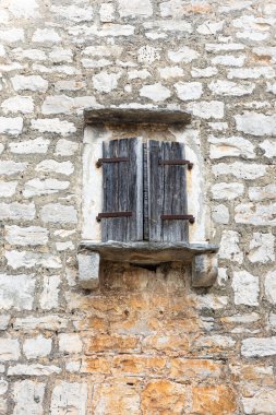 A weathered pair of wooden shutters covers an old stone wall, featuring rusted hinges and chipped paint. The aged texture evokes rural charm, history, and a sense of quiet, timeless decay.