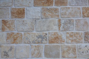A weathered gray stone wall built from irregular rocks, showing layered masonry and hints of dry grass in the foreground. Ideal for rustic architecture, durability, and natural construction themes.