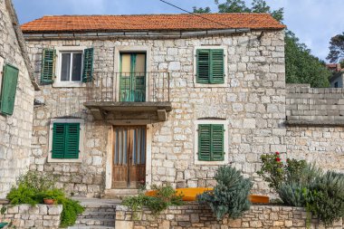 Dört ahşap panjurlu yıpranmış taş bir ev sessiz bir caddede oturuyor. Sert cephe, küçük kapı ve metal bisiklet rafları kırsal cazibeyi ve zamansız Akdeniz köyü atmosferini çağrıştırıyor..