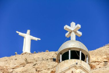 Bitkilerle bezenmiş kayalık bir yamacın canlı görüntüsü, aşağıdaki bir köy, engin masmavi gökyüzünün altında sakin ve doğal bir ortam..