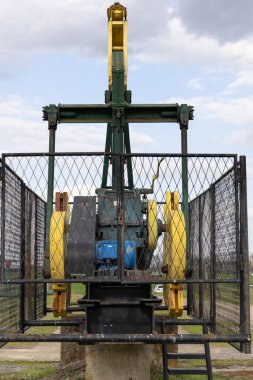 Petrol çıkarma için endüstriyel ekipmanlar bulutlu bir arka planda çitle çevrili bir alanda sergileniyor. Görüntü, makinenin işlevselliğini ve engebeli tasarımını vurguluyor, enerji altyapısı ve doğal kaynak endüstrilerini vurguluyor.