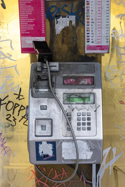 SPLIT, CROATIA, 10.25.2025: Yıpranmış bir ankesörlü telefon, afişler ve renkli etiketlerle çevrili, grafiti kaplı sarı bir duvarın karşısında oturuyor. Retro cihaz, sarmalanmış kablo, ve yontulmuş metal cesur şehir hayatı estetiğini ortaya çıkarıyor..