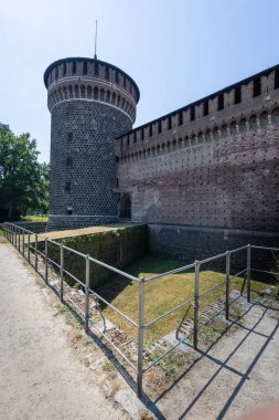 Kuru hendeğe tepeden bakan tuğladan bir kale duvarının yanında uzun yuvarlak bir taş kule duruyor. Parlak gün ışığı antik taş ustası ve tarihi kaleleri vurguluyor.