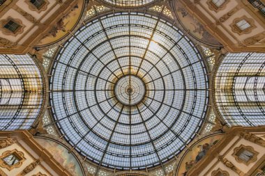 Süslü mimari detaylarla çerçevelenmiş büyük dairesel bir cam kubbenin çarpıcı yukarı bakan görüntüsü. Güneş ışığı ızgaranın içinden süzülerek, dekoratif motifleri zamansız, zarif bir iç ayarda vurguluyor.