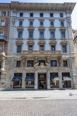 MILAN, ITALY, 06.19.2025: detaylı kornişler ve heykeltraş evleri olan büyük beyaz bir taş bina Gutteridge, lüks bir mağaza önü. Klasik mimari, uzun pencereler ve parlak bir şehir ortamı prestijli, zamansız bir ticari str oluşturur.