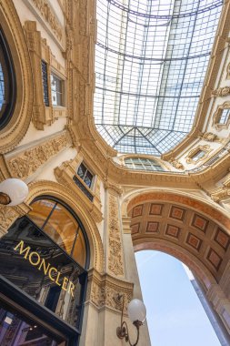 MILAN, ITALY, 06.19.2025: Milans ikonik galerisinde altın yaldızlı detaylar, cam bir kubbe ve butik mağazalar içeren zarif bir atari salonu. Moda, seyahat ve kentsel mimari görseller için idealdir.