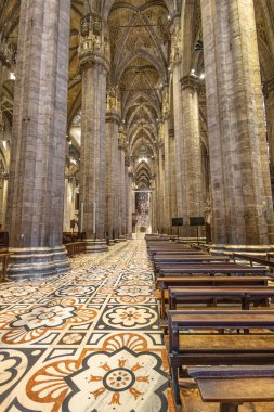 Büyük bir Gotik katedralin iç manzarası. Yüksek taş sütunlar, karmaşık mahzenler ve renkli camlar. Ahşap sıralar desenli döşeme döşemesi, sessiz bir yansıma ve korku uyandırıyor.