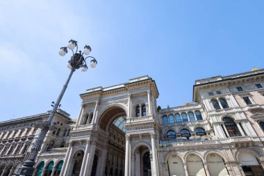 MILAN, ITALY, 06.19.2025: Büyük bir sokak kemeri ve cam atari salonu dramatik bir görünüm, süslü tarihi cephelerle çevrili. Parlak güneş, mimariyi, şehir ölçeğini ve gün ışığını vurgulayan bir yıldız patlaması yaratır..