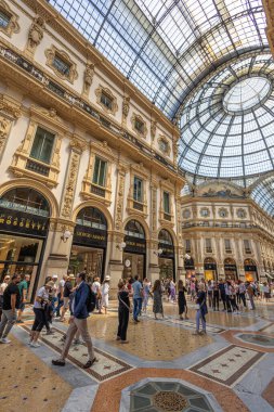 MİLAN, İtalya, 06.19.2025 Milans tarihi Galleria Vittorio Emanuele II 'nin içinde şaşaalı bir cam kubbe ile taçlandırılmış lüks bir alışveriş salonu olan süslü püslü gölgelerin altında yürüyen müşteriler ve ziyaretçiler.