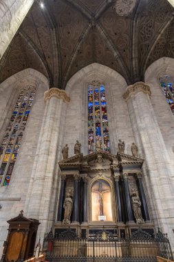 Büyük bir katedralin içinde uzun taş sütunlar, karmaşık kemerler ve renkli vitraylı pencereler var. Süslü bir sunak ve heykeller bu tarihi Gotik kilisede kutsal ve ilham verici bir atmosfer yaratıyor..