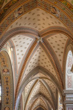 Tarihi bir kilise içinde renkli geometrik desenler, kemerler ve dekoratif motiflerle dolu karmaşık bir tavan. Zenginlik kutsal mekanı, ortaçağ mimarisini ve zamansız iç tasarım cazibesini çağrıştırıyor..