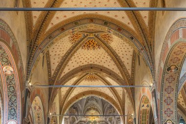 Tarihi bir kilise içinde renkli geometrik desenler, kemerler ve dekoratif motiflerle dolu karmaşık bir tavan. Zenginlik kutsal mekanı, ortaçağ mimarisini ve zamansız iç tasarım cazibesini çağrıştırıyor..