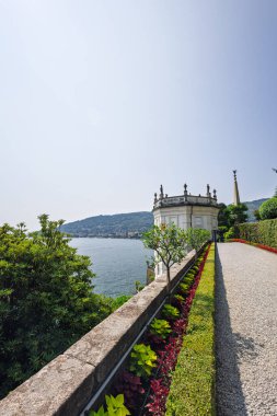 Bereketli bitkilerle çevrili sakin bir göl yolu, solda ve uzak tepelerde sakin suların oluşturduğu tarihi bir mermer pavyona ve dikilitaşa götürür. Zarif, sakin bir manzara yaratır..