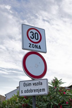 30 bölge hız sınırı işareti, dairesel giriş yasağı işareti ve bir Hırvat metin paneli olan bir sokak sahnesi. Yol güvenliğini, trafik kurallarını ve günlük şehir seyahatlerini sağlar..