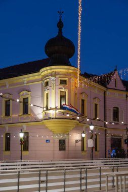 Alacakaranlık 'ta büyüleyici bir şehir manzarası. Pembe bir köşe binası, tel lambaları, kubbeli bir kule ve bayraklar. Sokak lambalarının sıcaklığı sessiz bir Avrupa caddesinde şenlikli bir atmosfer yaratır..