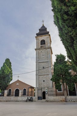 Huzurlu bir cadde boyunca uzanan uzun yeşilliklerin arasından yükselen tarihi bir çan kulesi klasik mimari cazibeyi ve sakin, güneşli şehir manzarasını yakalıyor..