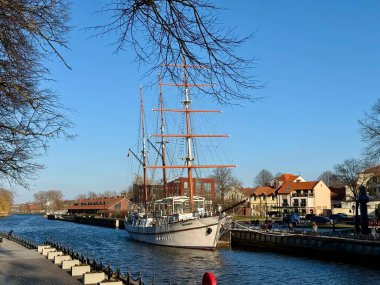 Meridiana yelkenli gemisi Litvanya 'nın Klaipeda kentinde sakin mavi bir su yoluna yanaştı. Gemi, karmaşık donanımlı, kırmızı-kahverengi renklerde uzun direkler içeriyor.. 