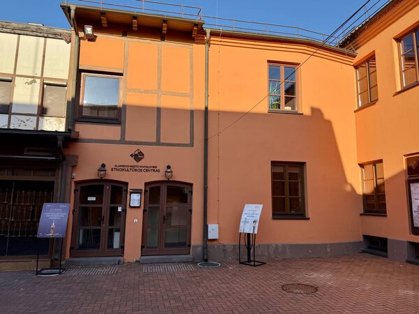 Klaipeda City Municipality Ethnocultural Center in Lithuania features a two-story building with peach-colored walls and brown-framed windows. It has a sign indicating its name above the entrance