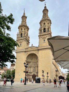 İspanya 'nın Logroo kentindeki Santa Mara de la Redonda Katedrali' nde ikiz Barok kuleleri ve karmaşık kabartmalarla süslenmiş büyük bir taş perdeler yer alıyor. Bina asfalt bir meydanda ayakta duruyor ve insanlar yürüyor ya da yakınlarda duruyorlar..