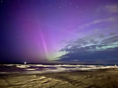 Görüntü, Letonya 'nın Liepaja kentindeki Baltık Denizi üzerinde kuzey ışıklarını yakalıyor. Gökyüzü mor ve yeşil auroraların canlı renkleriyle dolu. Ufuk boyunca uzanıyor.. 