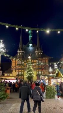 Bir el, ağaç ve evin beyaz tasarımlarının yer aldığı şenlikli bir kupayı tutuyor. Arka planda, Wernigerode, Almanya 'nın aydınlatılmış Noel pazarı