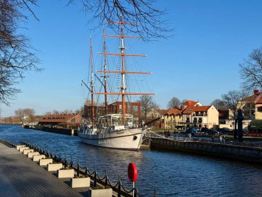 Üç direkli yelkenli gemi Litvanya, Klaipeda 'daki Dane Nehri boyunca demirledi. Ahşap gemi zincire bağlı korkuluklar ve beton direklerle kaplı asfalt bir geçitin yanında demirli. Yapraksız ağaçlar sahneyi çerçeveler