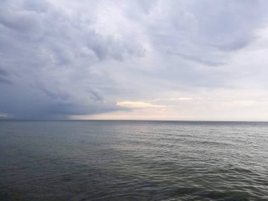 Dalgalar Karkle, Litvanya 'daki Baltık Denizi kıyısına doğru akıyor. Ufuk denizi parçalı bulutlu gökyüzünden ayırır, mavi ve gri renkleri harmanlar. Su kıyıya yakın sakin görünüyor, ince dalgalanmalar görülebiliyor..
