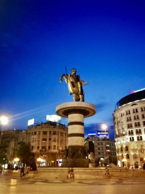 Üsküp 'ün tarihi merkezi Makedonya' da belirgin bir şekilde duran binicilik heykeli, koyu mavi bir akşam gökyüzüne karşı aydınlatıldı. Heykel, ışıklarla süslenmiş büyük silindirik bir kaide üzerinde yükselir.,