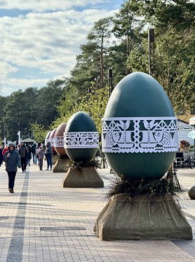 Büyük dekoratif Paskalya yumurtaları Litvanya, Palanga 'da yaya geçidi hizasında. Yumurtalar karmaşık bir şekilde beyaz dantel gibi dizaynlarla süslenmiş, sağlam tezgahlara kurulmuş. Geçit genç ağaçlarla çevrili. Taze yeşil yaprakları baharı gösteriyor..