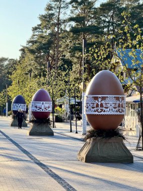 Litvanya, Palanga 'da sergilenen büyük dekoratif Paskalya yumurtası. Yumurta kırmızıya boyanmıştır ve geleneksel motiflere sahip, stilize ağaçlar ve hayvanlar da dahil olmak üzere karmaşık beyaz bir kağıt kesim bandına sahiptir. Çuval bezine sarılı bir üste