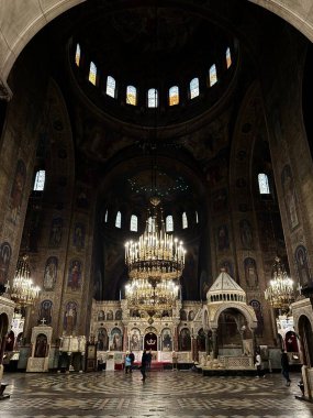 Bulgaristan 'ın Sofya kentindeki Saint Alexander Nevsky Katedrali' nin içi. Görüntü, dini fresklerle süslenmiş büyük merkez kubbeyi ve bir dizi kemerli vitray pencereleri sergiliyor. Tavandan büyük, süslü bir avize sarkıyor.