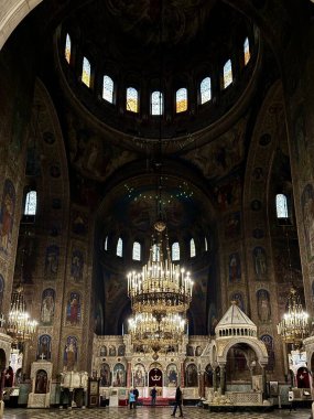 Bulgaristan 'ın Sofya kentindeki Saint Alexander Nevsky Katedrali' nin içi. Görüntü, dini fresklerle süslenmiş büyük merkez kubbeyi ve bir dizi kemerli vitray pencereleri sergiliyor. Tavandan büyük, süslü bir avize sarkıyor.