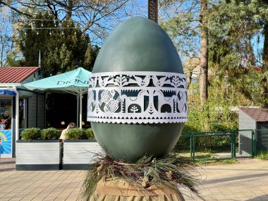 Litvanya 'nın Palanga kentinde büyük dekoratif bir Paskalya yumurtası, ortasında karmaşık beyaz bir şerit bulunan koyu yeşil bir yüzeye sahiptir. Grup geleneksel desenleri kuş ve çiçek motifleriyle sergiliyor. Yumurta bir üste duruyor.