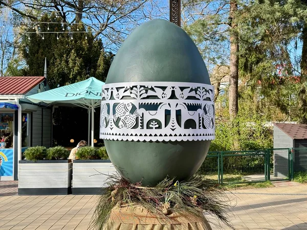 Litvanya 'nın Palanga kentinde büyük dekoratif bir Paskalya yumurtası, ortasında karmaşık beyaz bir şerit bulunan koyu yeşil bir yüzeye sahiptir. Grup geleneksel desenleri kuş ve çiçek motifleriyle sergiliyor. Yumurta bir üste duruyor.