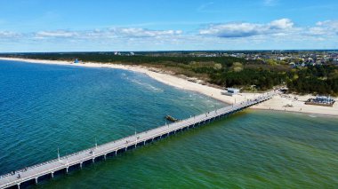 Litvanya 'nın Palanga kıyı şeridi boyunca Baltık Denizi' nin hava manzarası. Görüntüde denize doğru uzanan ve kumlu plajlarla çevrili ve yemyeşil ormanlarla bezenmiş uzun bir ahşap iskele yer alıyor. Deniz suyunun mavi ve yeşil tonları vardır..