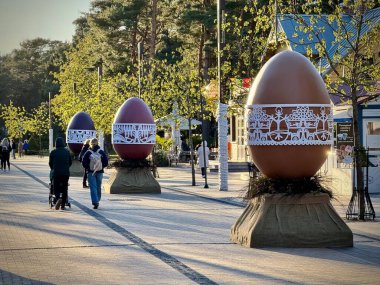 Süslü dev Paskalya yumurtaları Litvanya 'nın Palanga kentindeki asfalt bir patika boyunca sergilenir. Her yumurta karmaşık beyaz dantel desenlerle bezenmiş, binalar görünür durumda, Paskalya kutlamalarındaki hareketli sokak manzarasını güçlendiriyor..