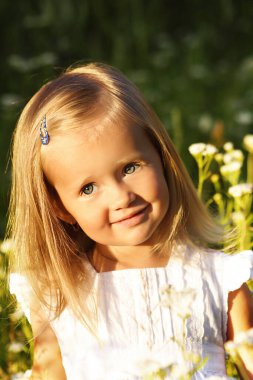 Sarışın çocuk yazın çiçek tarlasında gülümsüyor