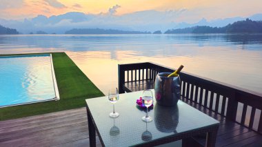 Sonsuzluk havuzuna bakan iki bardak ve şişe masa ve gün batımında Cheow Lan Gölü, Khao Sok Ulusal Parkı, Tayland, Güneydoğu Asya.