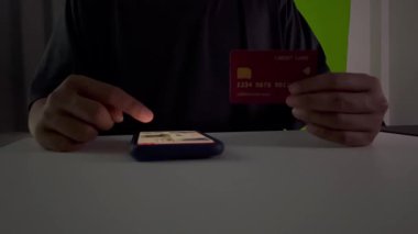 Asyalı bir adam gecenin karanlığında kredi kartı ve akıllı telefonuyla işlem yapıyor. Pazar yerinde kredi kartıyla alışveriş yapmak..