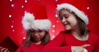 Noel Baba şapkalı iki tatlı kız Noel arkaplanındaki hediyeleri açıyor.