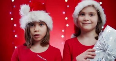Noel Baba şapkalı iki tatlı kız Noel arkaplanındaki hediyeleri açıyor.